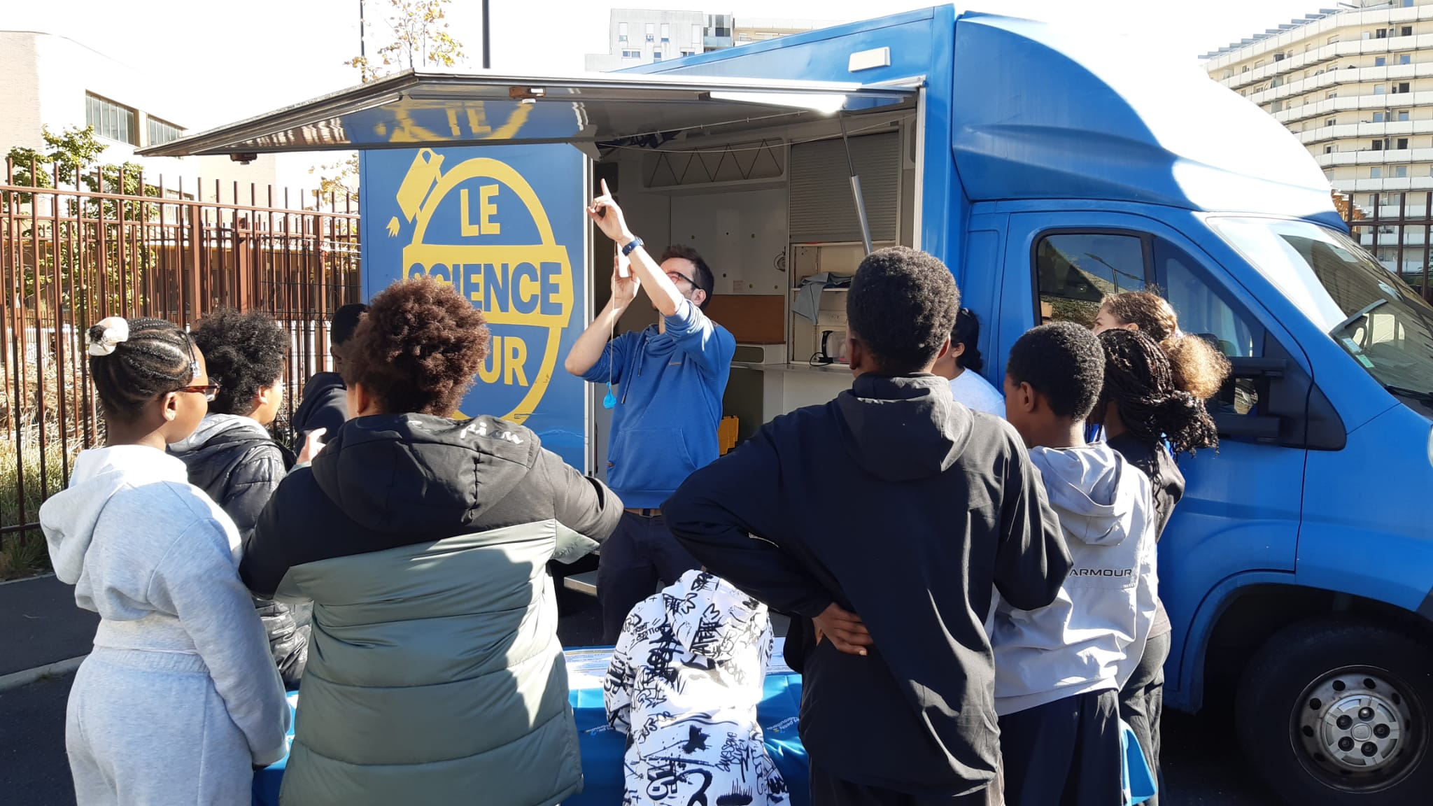 Un groupe participe à une animation scientifique devant le camion bleu du Science Tour.